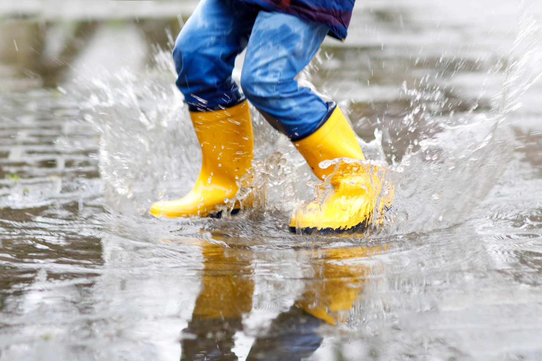 Illustrasjonsfoto av et barn som hopper i en vanndam med gule støvler. Foto: Mostphotos